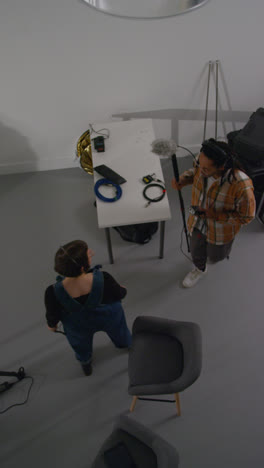 Vertical-Video-Overhead-Shot-Of-Sound-Recordist-And-Production-Assistant-Working-On-Film-Set-Shooting-Movie-Or-Video-In-Studio